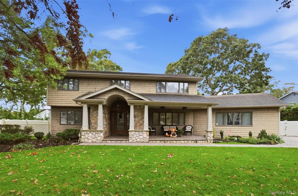 Two-story shingle-style exterior featuring a covered front porch with stone pillars, a stone-accented entryway, and a paved walkway
