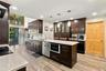 Kitchen featuring dark wood cabinetry, light-toned stone countertops, a central island with integrated microwave, wood-finish flooring, and pendant li