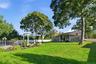 Expansive backyard featuring a sprawling lawn, mature trees, an inground pool with metal perimeter fencing, and a white architectural pergola