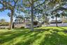 Expansive backyard featuring mature hardwood trees, a manicured lawn, full-height privacy fencing, and a multi-pane glass sunroom addition
