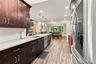 Kitchen featuring stained wood cabinetry, stone countertops, white subway tile backsplash, wood-finish flooring, and stainless steel appliances
