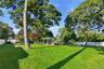 Expansive backyard featuring a white pergola, detached storage structure, mature trees, and perimeter fencing