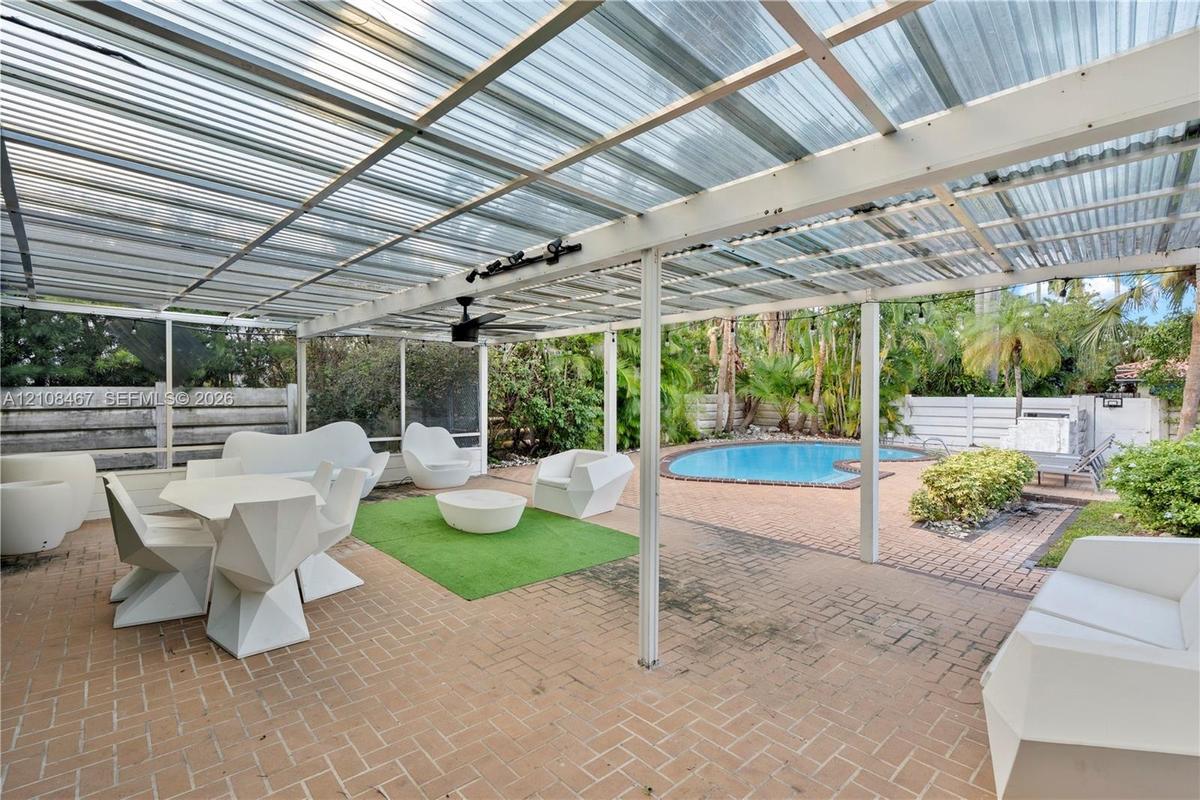Covered outdoor patio featuring a corrugated translucent roof, integrated ceiling fan, and brick paver flooring, complete with a screened enclosure an