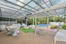 Covered outdoor patio featuring a corrugated translucent roof, integrated ceiling fan, and brick paver flooring, complete with a screened enclosure an