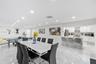 Large-format tile flooring, recessed ceiling lighting, and a kitchen featuring a stone-finish waterfall edge peninsula, white cabinetry, and stainless