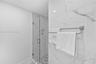 Shower featuring large-format veined wall tile, glass enclosure, built-in wall niche, and pebble-finish floor tile