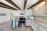 Kitchen featuring exposed wood ceiling beams, solid-surface countertops, white cabinetry, and stainless steel range