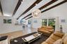 Vaulted ceiling with exposed wood beams, tile flooring, large-scale pendant lighting, and oversized windows