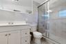 Bathroom featuring a white vanity cabinet, large wall-mounted mirror, walk-in shower with sliding glass doors, and light-toned tile wall finishes