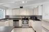 Kitchen featuring cabinetry with white shaker-style doors, stone-finish countertops, stainless steel appliances, ceramic tile backsplash, and ceramic 