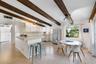 Exposed dark wood ceiling beams, tile flooring, white cabinetry, integrated peninsula, and track lighting