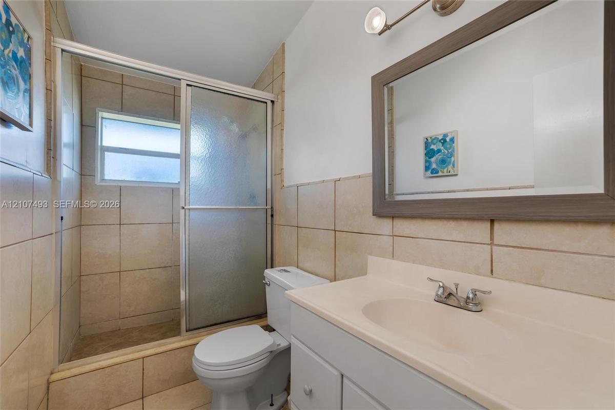 Bathroom featuring a vanity with an integrated basin, a framed wall mirror, a tiled shower enclosure with sliding glass doors, and light-toned wall ti