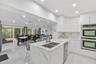 Kitchen featuring white flat-panel cabinetry, stone-patterned countertops, a central island with a double-basin stainless steel sink, built-in double 