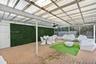 Covered patio featuring a corrugated translucent roof, brick paver flooring, green decorative privacy wall, ceiling fan, and white structural support 