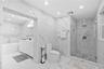 Full-height wall-to-wall stone-finish tile, glass-enclosed shower with pebble-finish flooring, built-in recessed wall niche, freestanding soaking tub,