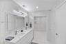 Dual-sink vanity with white countertop, full-width mirror, integrated wall-mounted lighting, floor-to-ceiling stone-look wall tiling, and walk-in show