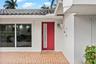 Red entry door with vertical frosted glass insert, terracotta brick patio, white stucco exterior, and barrel tile roof