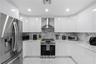 Modern kitchen featuring high-gloss white cabinetry, stone-surface countertops, full-height stone backsplash, stainless steel appliances, and large-fo