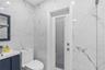 Full-height wall tiling with a veined pattern, vanity featuring a rectangular integrated sink, solid-color cabinetry, and a door with an integrated pr