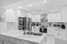 Modern kitchen featuring high-gloss white cabinetry, stone countertops and backsplash, stainless steel built-in double ovens, stainless steel range ho