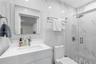 Bathroom featuring large-format wall tiling with veining detail, glass-enclosed shower with a rainfall showerhead, vanity with integrated basin, and m