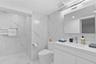 Bathroom featuring floor-to-ceiling large-format tile with marble-pattern finish, vanity with integrated sink and countertop, frameless wall-mounted m