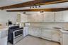 Kitchen featuring white cabinetry, solid-surface countertops, stainless steel range, integrated dishwasher, and exposed wood ceiling beams