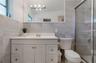 Bathroom featuring a white vanity cabinet, solid-surface countertop with integrated sink, large-format tile wall cladding, full-width mirror, and a gl