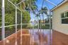 Screened lanai featuring tile flooring, a metal frame enclosure, and a backdrop of mature palm trees and water