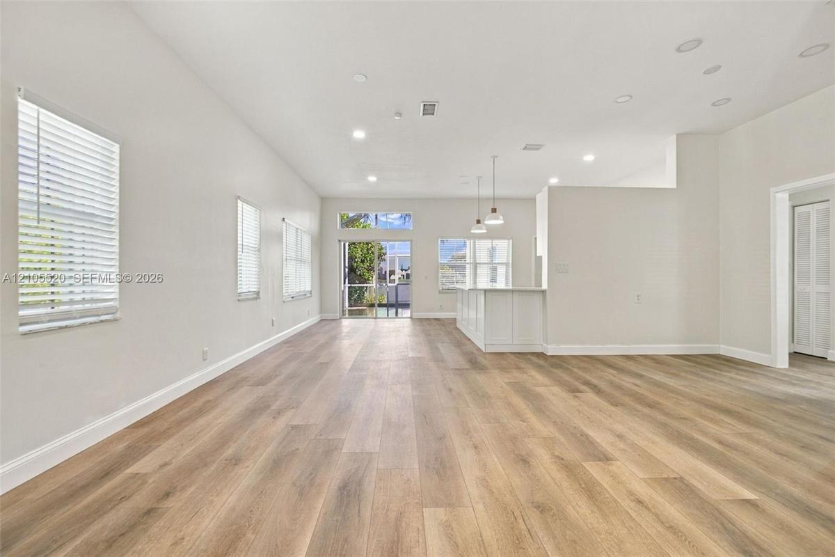 Open-concept interior featuring wood-finish flooring, recessed lighting, white cabinetry, pendant lighting, and glass sliding doors