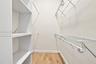 Walk-in storage space featuring wood-finish flooring, white laminate shelving towers, and white wire rack shelving with integrated hanging rods