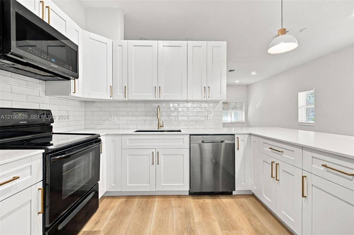 Kitchen featuring white shaker cabinetry, quartz countertops, subway tile backsplash, stainless steel appliances, and wood-finish flooring