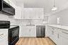 Kitchen featuring white shaker cabinetry, quartz countertops, subway tile backsplash, stainless steel appliances, and wood-finish flooring