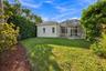 Rear exterior featuring a screened-in lanai, concrete tile roof, manicured lawn, and perimeter landscaping