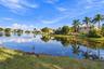 Waterfront property featuring a manicured lawn, mature palm trees, and a lake