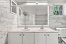 Double vanity featuring a stone countertop, dual undermount sinks, large rectangular mirror, and full-height stone-finish wall tile with accent inlay