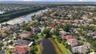Aerial perspective of a multi-story residence featuring a tile roof, situated on a lot bordering a community pond with mature landscaping and palm tre