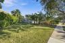 Expansive lawn area featuring mature palm trees, dense peripheral privacy hedging, and a paved concrete walkway
