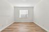 Neutral interior space featuring wood-finish flooring, crisp white walls, and a single window with horizontal blinds