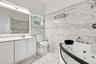 Bathroom featuring floor-to-ceiling large-format tile with stone-pattern finish, jetted soaking tub, white vanity cabinet with countertop basin, and o