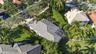Aerial perspective of a property featuring a multi-pitched tile roof, an enclosed screened lanai, mature landscaping, and an expansive lawn