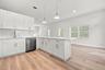 Kitchen featuring white shaker-style cabinetry, quartz countertops, a stainless steel dishwasher, subway tile backsplash, and wood-finish flooring