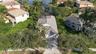 Aerial perspective featuring a concrete tile roof, paved driveway, enclosed rear patio, and mature landscaping on a waterfront lot