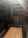 Walk-in closet featuring floor-to-ceiling built-in cabinetry, integrated shelving units, a four-drawer dresser cabinet, metal hanging rods, and wood-f