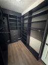 Custom walk-in storage featuring dark finish floor-to-ceiling cabinetry, integrated shelving, built-in dresser drawers, and wood-finish flooring