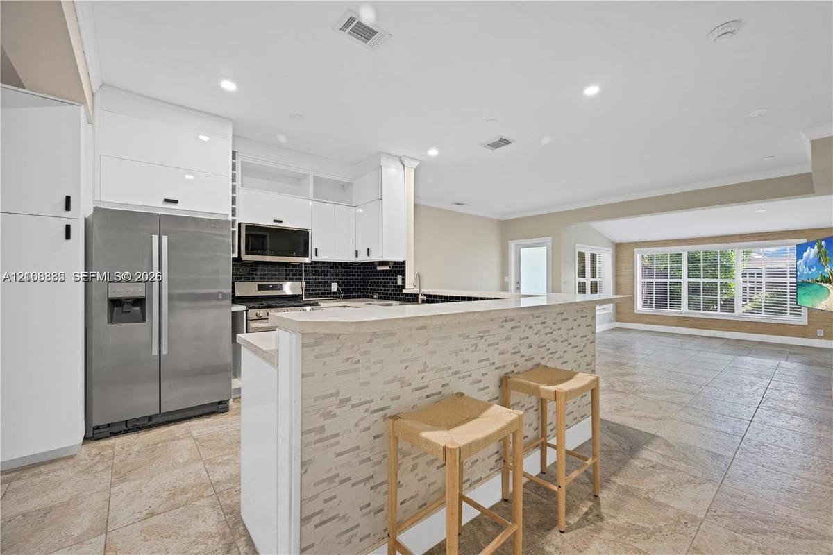 Kitchen featuring white flat-panel cabinetry, stainless steel appliances, a stone-tile breakfast bar, and tile flooring