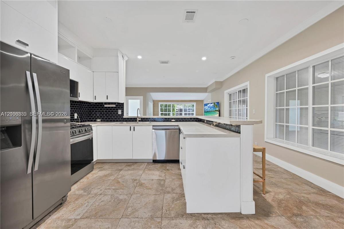 Kitchen featuring white shaker cabinetry, stainless steel appliances, a black tiled backsplash, a stone-finish countertop peninsula, and ceramic tile 