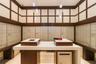 Custom built-in bar featuring a sleek waterfall edge countertop, integrated wood-finish cabinetry, recessed ceiling lighting, and polished stone floor
