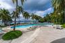 Outdoor patio featuring paved tile flooring, mature palm trees, string lighting, and an in-ground swimming pool overlooking the water
