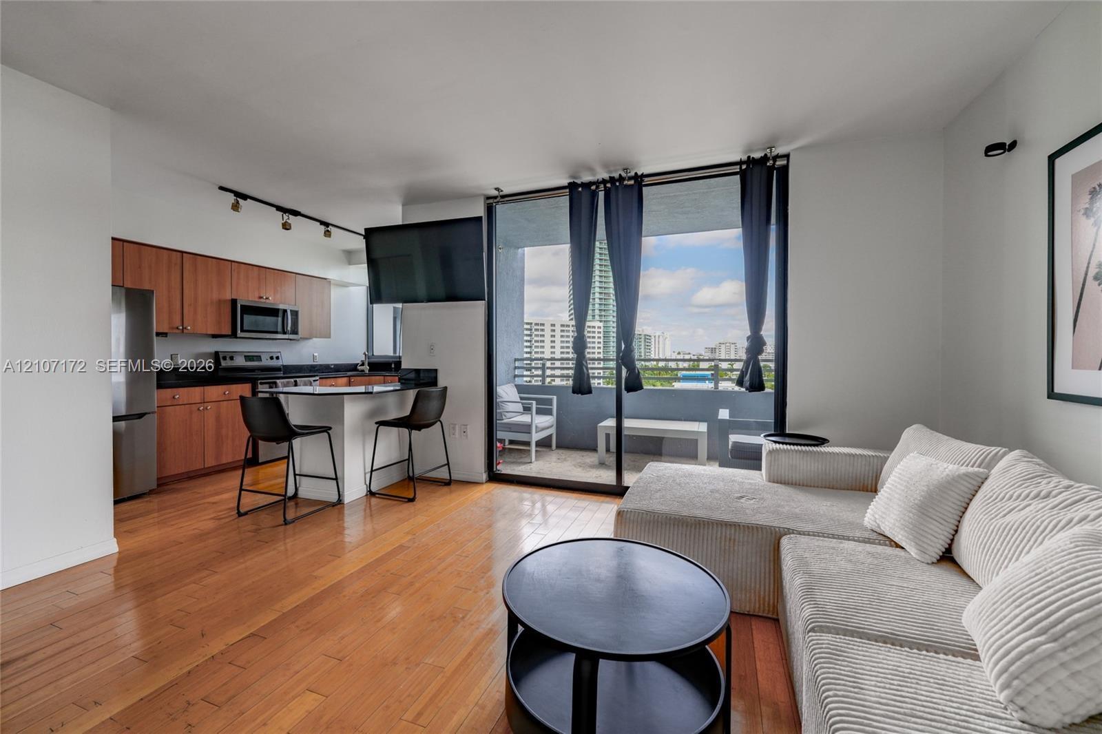 Open-concept kitchen featuring wood-finish cabinetry, stone countertops, and integrated stainless steel appliances, complemented by wood-finish floori
